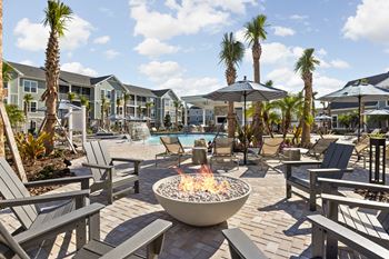 A fire pit sits in the middle of a patio surrounded by chairs and umbrellas.